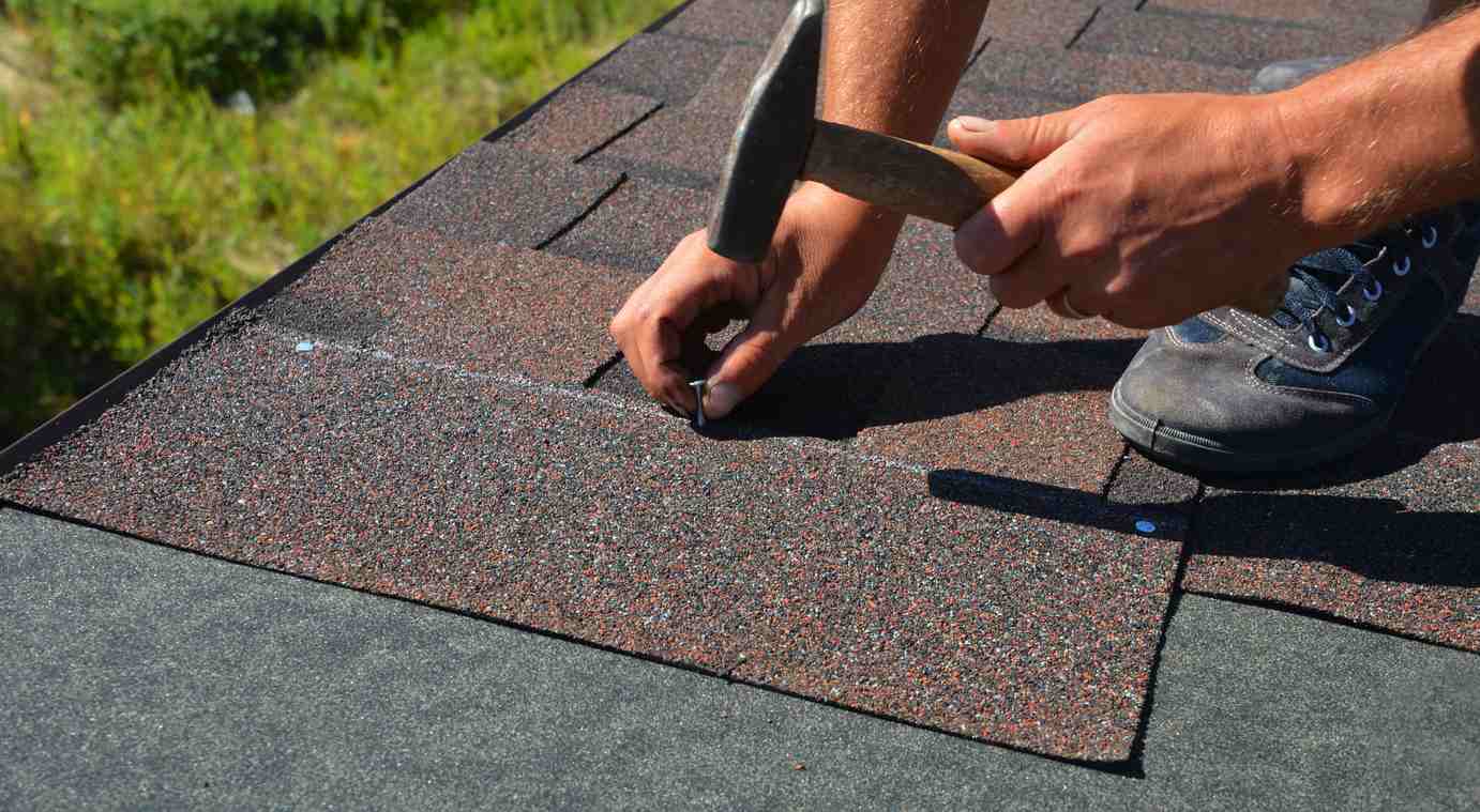 Man hammering composition shingles into a roof